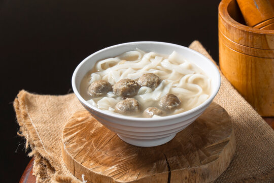 Savory Meatball Noodle Soup: A steaming bowl of flavorful noodle soup brimming with tender meatballs, served on a rustic wooden platform. A comforting and hearty meal.