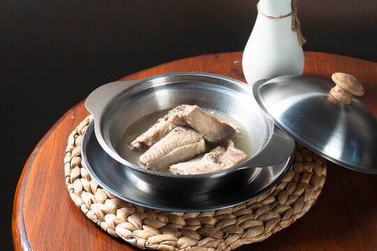 Canned Fish Dish: Delicious pieces of fish preserved in oil, served in a metallic bowl, accompanied by a small pitcher and a woven placemat, suggesting a simple, satisfying meal.