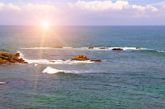 Beautiful Ocean Landscape with Rocky Reefs at Bright Sunset Scenic Sea Horizon with Crashing Waves and Sun Flare