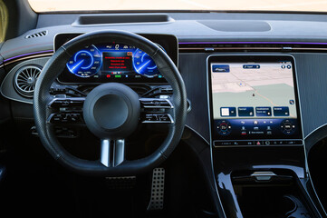 Naklejka premium Driver cockpit and dashboard of a modern luxury car with a perforated leather steering wheel, digital instrument cluster, and a large multimedia navigation display, close up.