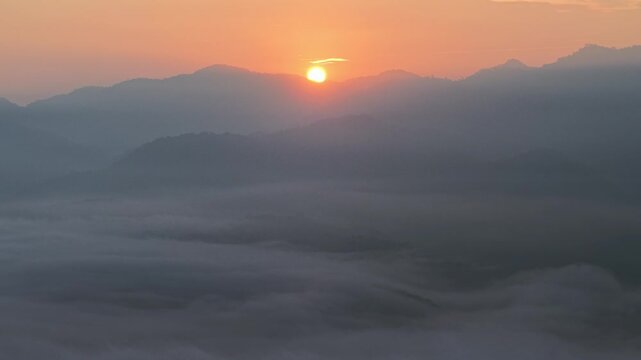 Sun rises above misty mountain peaks. Golden light fades across valleys. Fog swirls gently below at Lenggong, Malaysia