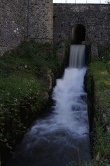 Cascada de agua bajo murallas de piedra del Castillo de Fougères en la Bretaña francesa © Eva