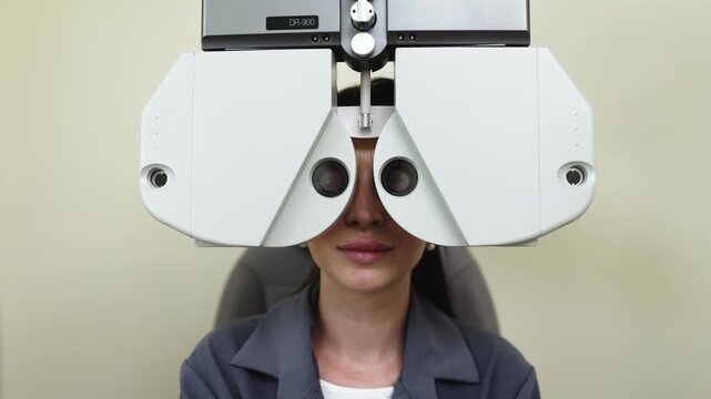 Female patient undergoing eye examination with phoropter device, adjusting lenses while seated in an optometry clinic, neutral background and soft lighting enhance focus on the procedure