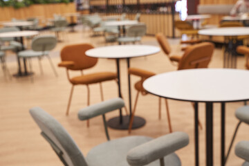 Fototapeta premium Empty Modern Cafe With Round Tables And Mixed Upholstered Chairs Arranged On Wooden Floor In Bright Open Seating Area Of Communal Dining Space.