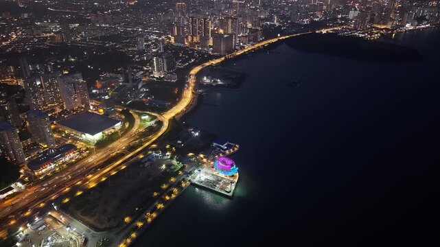 Drone aerial night shot of illuminated coastal gallery beside winding highway at Gelugor, Penang