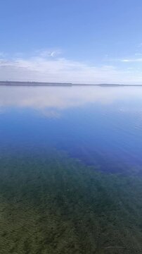 A clear lake with a sandy bottom and a wooden pier.