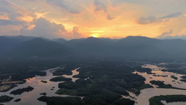 Aerial landscape of a winding river flowing through dense forest with mountains in the background at Tasik Raban