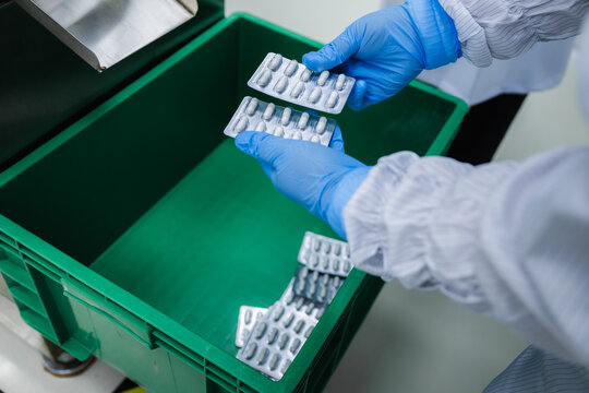 Close up factory worker hands holding pharmaceutical pill blister packs, concept of medicine quality control inspection in manufacturing plant