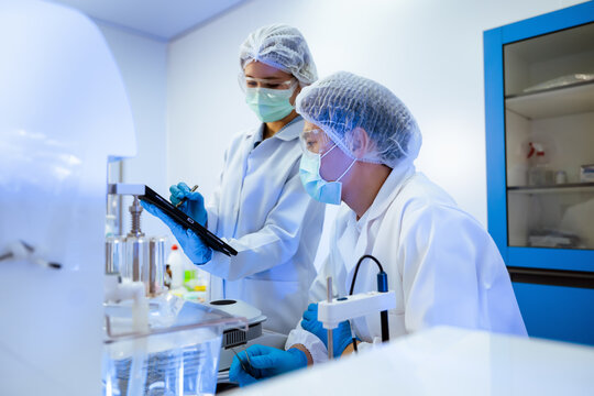 Asian scientists team checking pharmaceutical research data on digital tablet inside modern science laboratory concept of medical clinical development, Professional biotechnology experiment