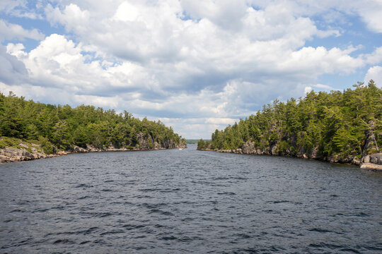 A distant view of Hole in the Wall from the 30,000 Islands cruise in Parry Sound, Ontario, showcasing lush greenery and serene waters under a partly cloudy sky.