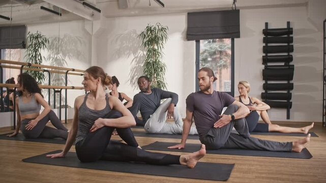 Group yoga class. Multicultural people doing yoga in hall. Multiethnic men and women in special yoga uniforms. Spiritual union with inner world. People sitting on mats and doing yoga exercise.