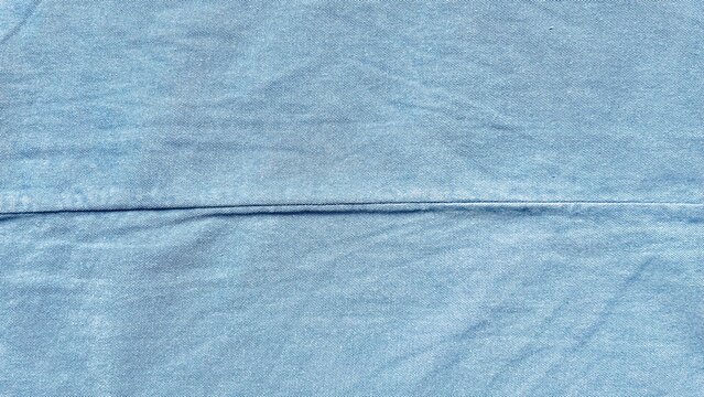 light blue denim fabric texture with horizontal seam showing natural weave pattern and soft washed cotton material background