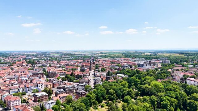 Spektakul&auml;re Weitwinkel-Luftaufnahme von Landau in der Pfalz unter blauem Sommerhimmel, die die dichte Altstadt, markante Kirchen und angrenzende gr&uuml;ne Parkanlagen zeigt.
