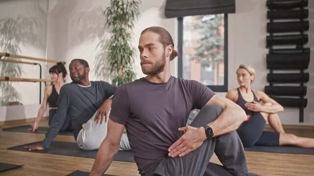 Group yoga class. Multicultural people doing yoga in hall. Multiethnic men and women in special yoga uniforms. Spiritual union with inner world. People sitting on mats and doing yoga exercise.