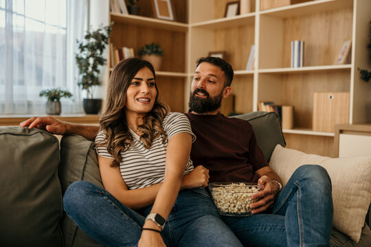 Couple watching movie and eating popcorn on sofa