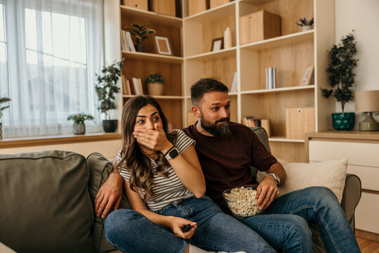 Couple watching scary movie with popcorn at home