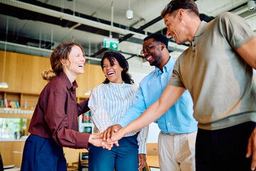 Fototapeta na wymiar Diverse business team stacking hands in a huddle, celebrating unity, collaboration, and shared success with happy expressions in an office