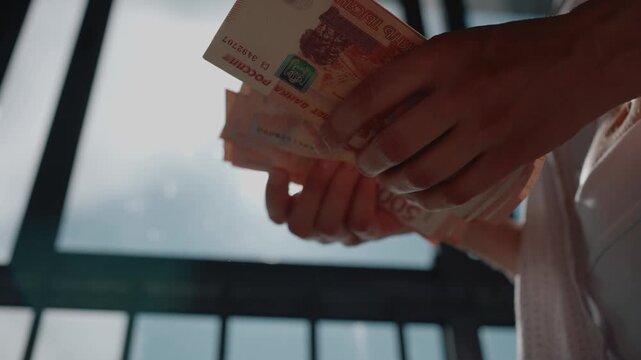 Close up of a business woman's hands counting a substantial stack of five thousand russian ruble bills with a sunlit window in the background, representing financial success and profit
