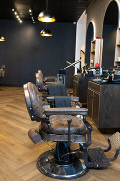 Vintage brown leather barber chair is sitting in barbershop aisle, showing worn headrest