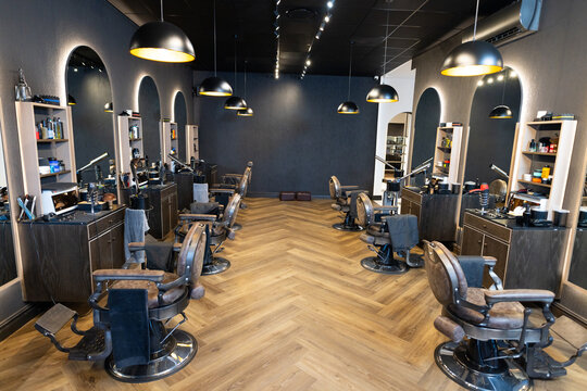 Leather barber chairs are lining central aisle in modern barber shop, showing vintage styling