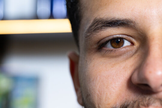 African man occupying right side of frame in living room, revealing brown eye, stubble, bookshelf