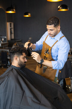 African American male barber trimming male client's hair with clipper in barbershop