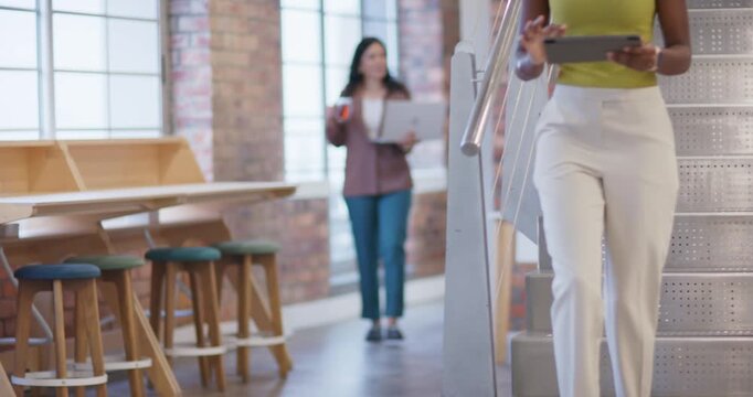 African American woman stepping down stairs at office in green top reading tablet, smiling