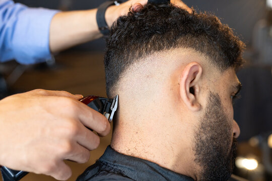 African American male barber trimming male client's hair in barber chair with cape and clipper