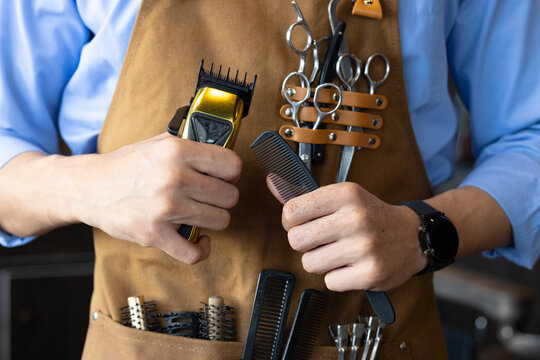 African American male barber gripping gold clipper, black comb at barbershop wearing leather apron