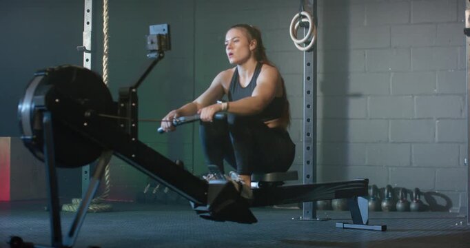 Adult woman starting at catch, pushing legs, pulling handle, rowing on rowing machine for fitness