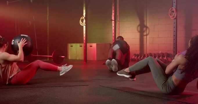 Diverse gymmates following left initiating twist, performing med-ball twists in gymwear for core