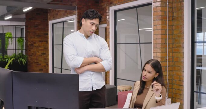 Diverse team handling project issue at desk, Asian man pointing at monitor, woman answering phone