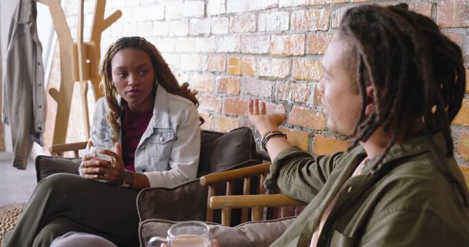 African American friends talking on sofa man starting speaking  and  gesturing, woman holding glass 