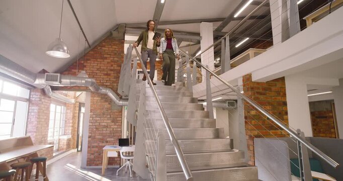 African American coworkers stepping onto stairs in loft using tablet discussing window seating