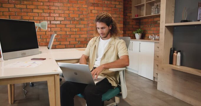 Man spotting pages, sitting in chair at brick office using laptop, reviewing charts for report