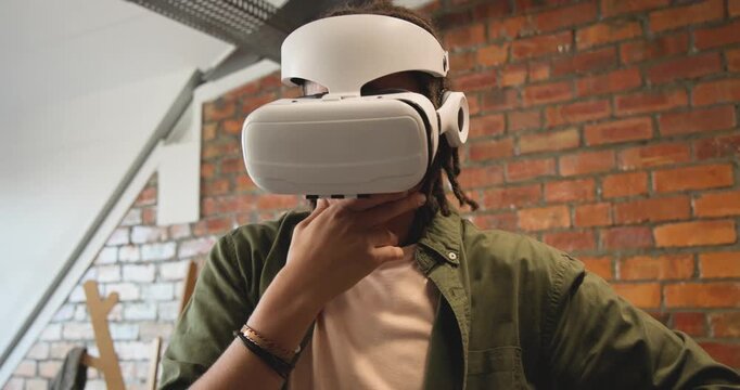 African adult male testing VR, assessing fit, adjusting headset, reaching at virtual items in loft