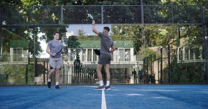 Two adult men warming up on blue paddle court, right man stepping forward tapping paddle