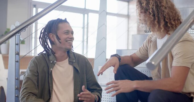 African American men taking break from work, talking and laughing on office stairs by windows