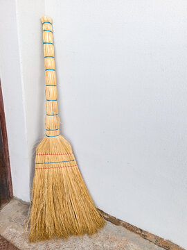 Traditional sorghum straw broom standing against white wall