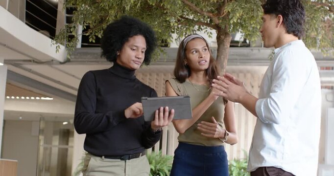 Diverse coworkers in open atrium, speaker starting explanation, tablet tapping, reviewing project