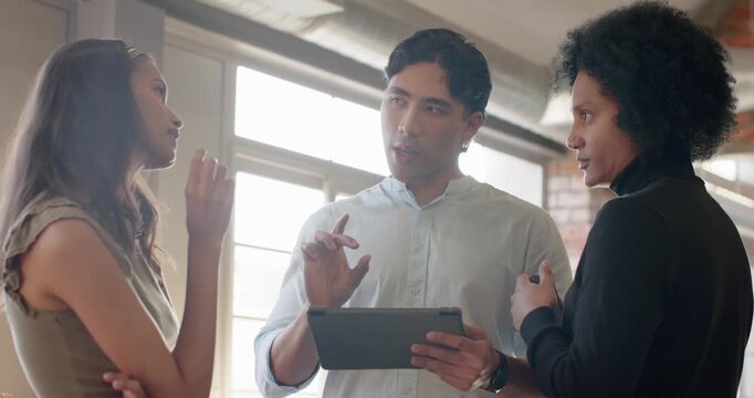 Diverse coworkers by window discussing tablet, exchanging gestures and counterpoints for review