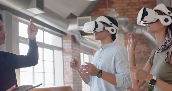 Diverse team using white VR headsets in loft, trainer entering left with tablet guiding VR training