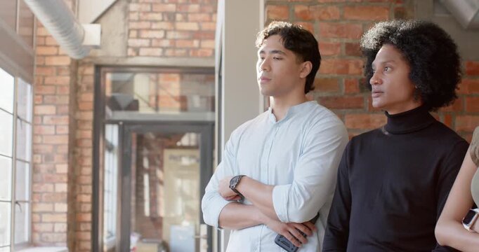 Diverse team lining by loft windows as peer coming from right, gazing as sunlight brightening phone