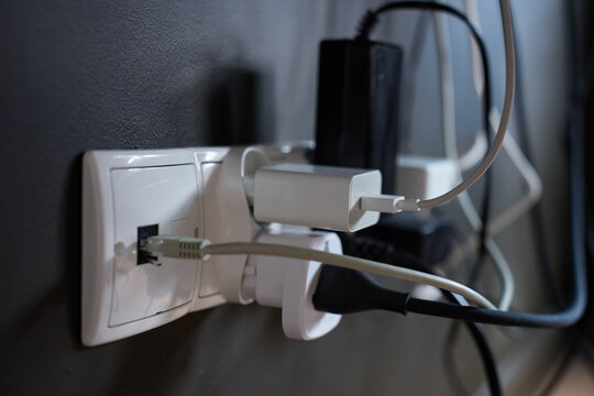 Multiple chargers and cables connected to wall socket behind electronic equipment