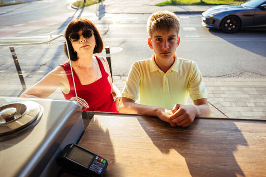 Mature mother and teenage son ordering ice cream together at sunny street kiosk in summer city