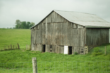 Weathered abandoned barn in the rolling countryside of rural Kentucky surrounded by green pasture © Yuliya