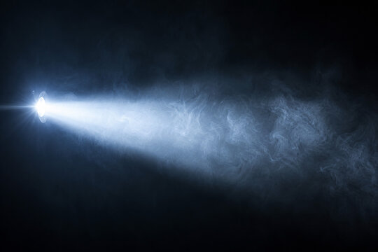 Bright blue spotlight ray illuminating smoke against dark black background.