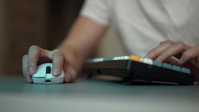 Young male gamer, streamer playing online video games at night on mechanical keyboard with colorful backlighting. Concept of intense focus and quick reflexes on mouse and keys, close-up, slow motion.