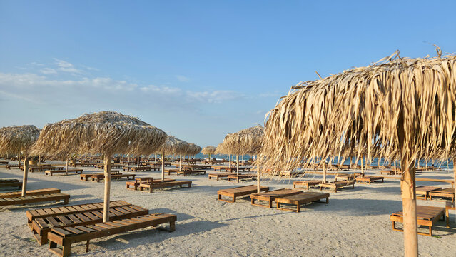 Row of straw beach umbrellas and wooden loungers on sandy beach
