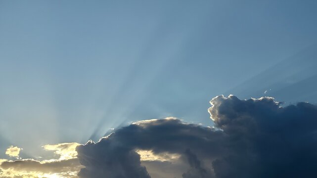 Sunlight rays piercing through dark clouds in blue sky